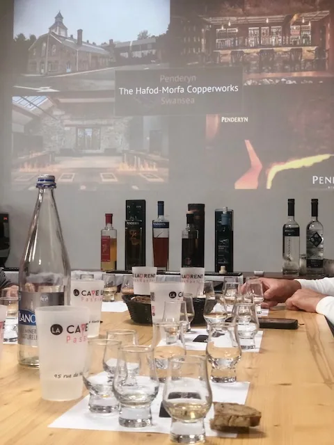 Projection d'images d'une distillerie pendant une dégustation, bouteilles et verres alignés sur la table
