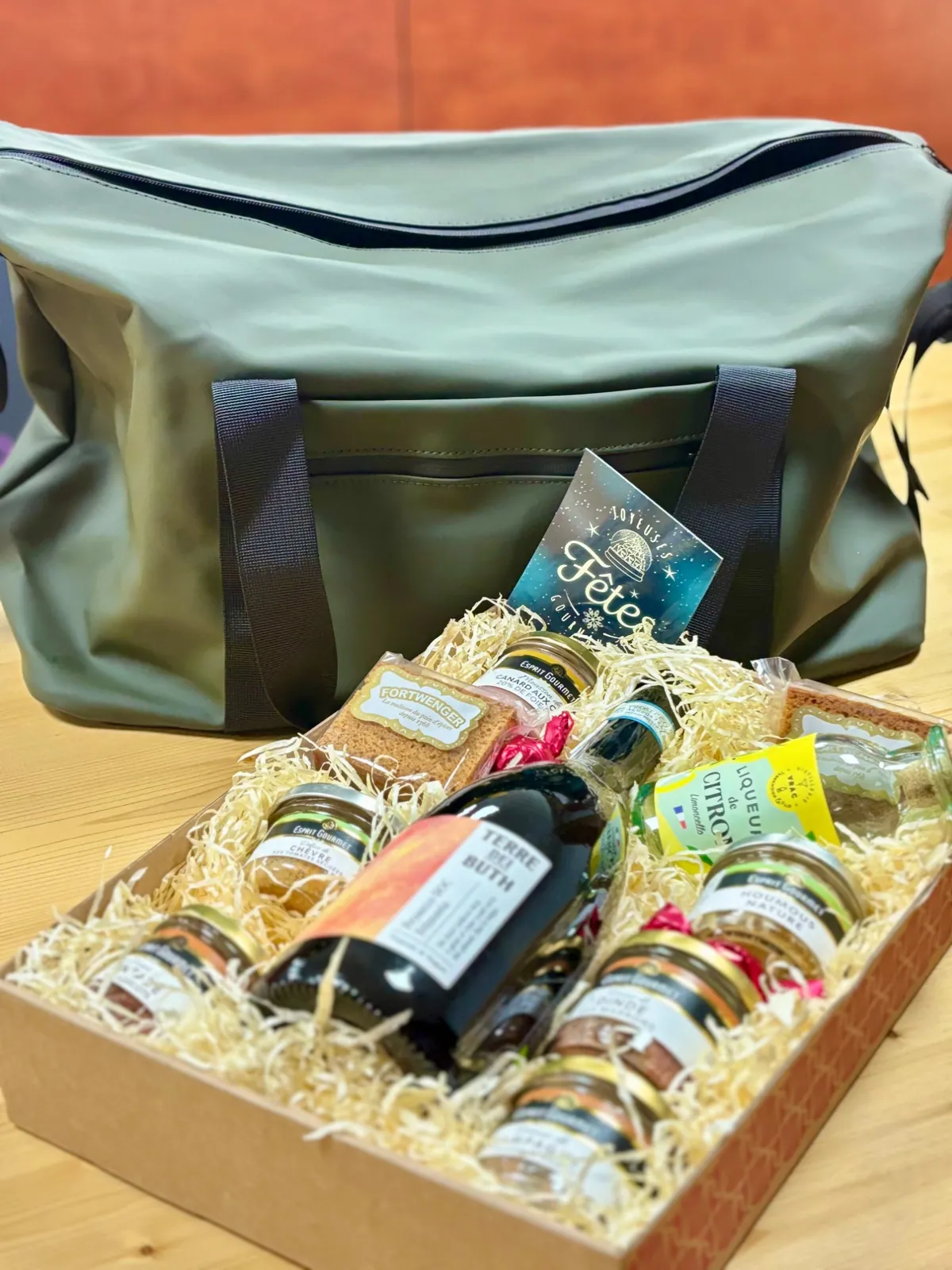 Coffret cadeau garni de produits gourmands et de vin, devant un sac étanche vert personnalisable